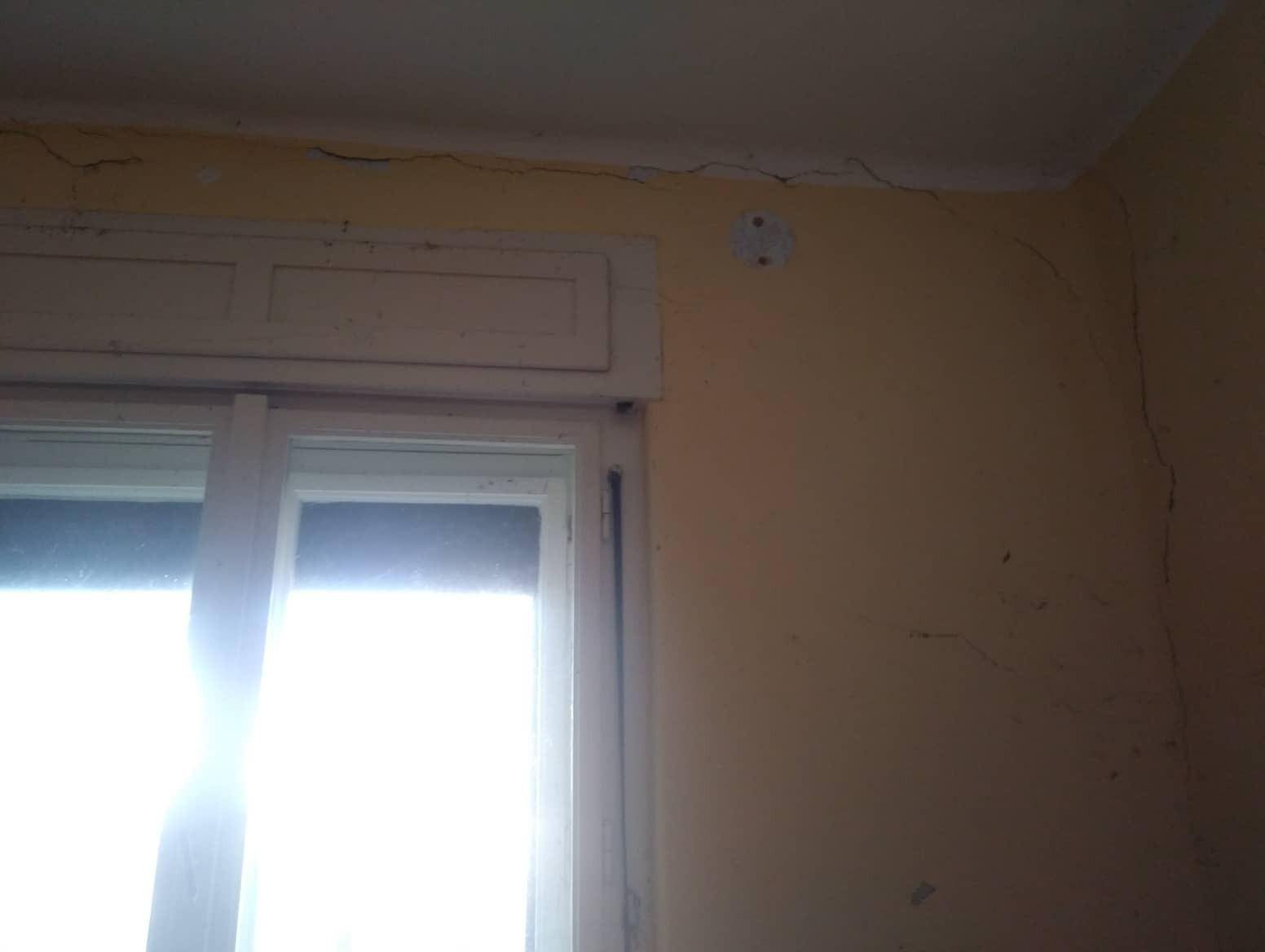 Innenansicht eines Fensters mit Rollladen und Rissen an Wand und Decke, die Renovierung erfordern.