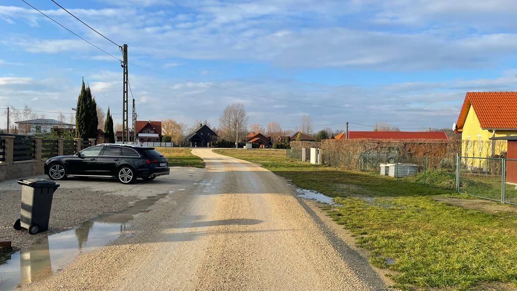 Ländliche Zufahrtsstraße mit geparktem Auto und weiteren Häusern in der Ferne.
