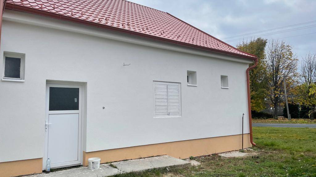 Seitenansicht des Hauses mit weißer Fassade, rotem Dach und einem kleinen Eingangsbereich.