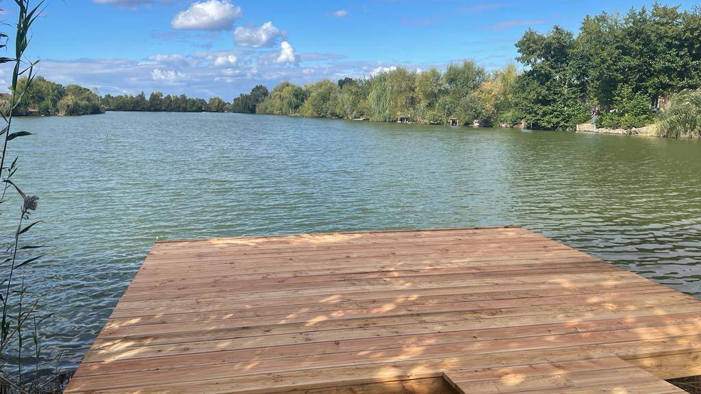 Weitläufiger Blick über den See von einem neuen Holzsteg aus unter einem strahlend blauen Himmel.