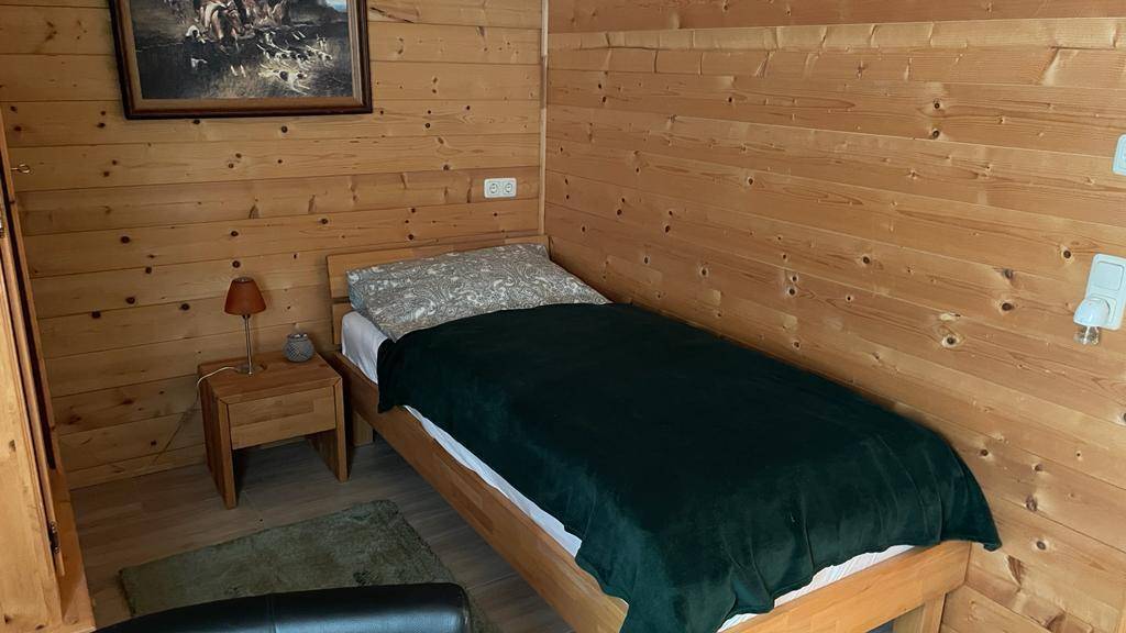 Schlafzimmer mit Einzelbett und Holzwänden, einfach und funktional eingerichtet.