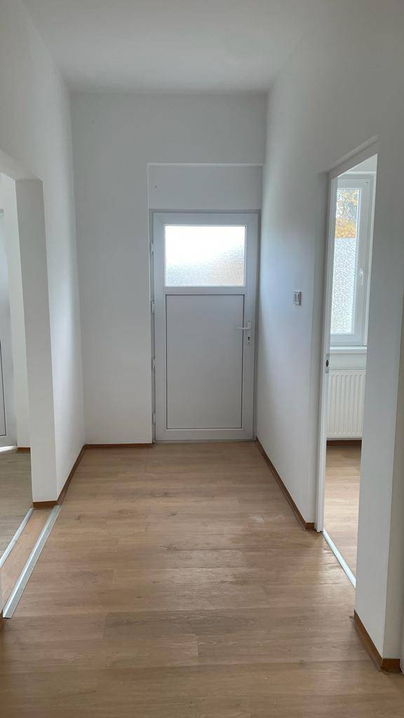 Heller Flur mit Laminatboden, weiß gestrichenen Wänden und einer Eingangstür.