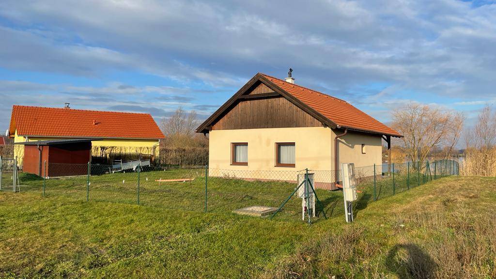Kleines Haus mit Ziegeldach und umzäuntem Grundstück in ländlicher Umgebung.