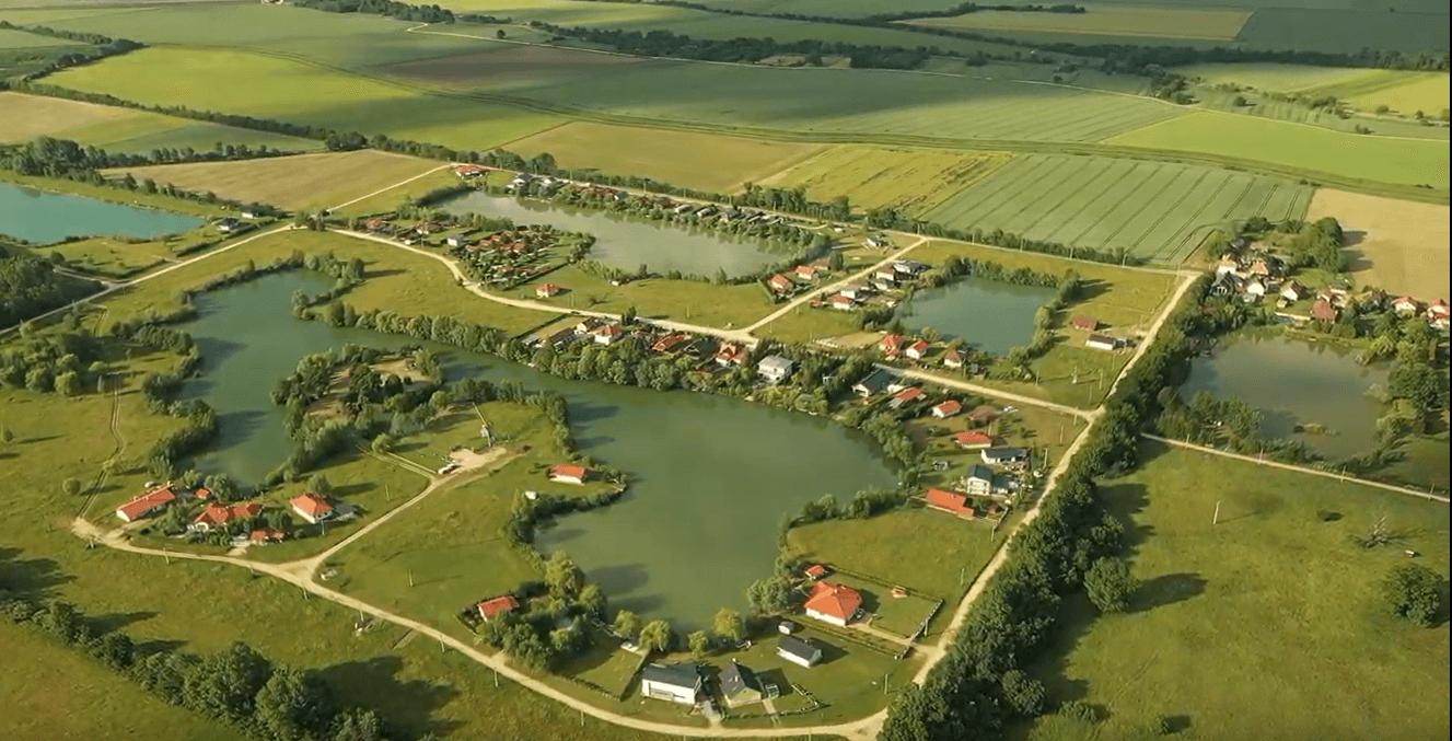 Detailreichere Luftaufnahme der Seen und umliegenden Häuser in der grünen Landschaft, gut beleuchtet.
