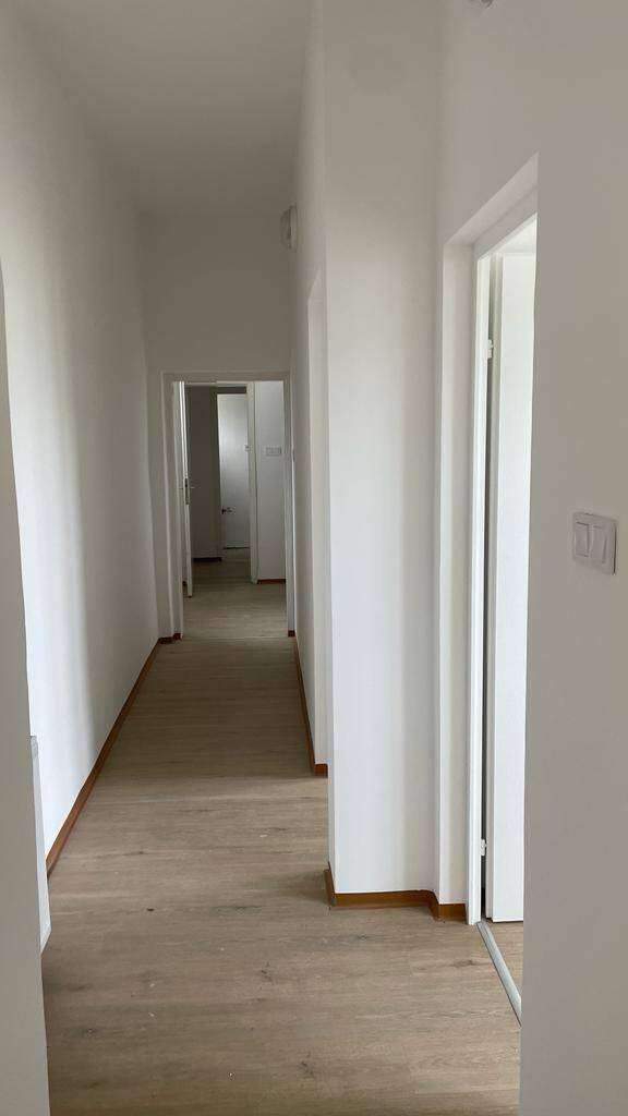 Langer Flur mit Laminatboden, weißen Wänden und mehreren Türen zu angrenzenden Räumen.
