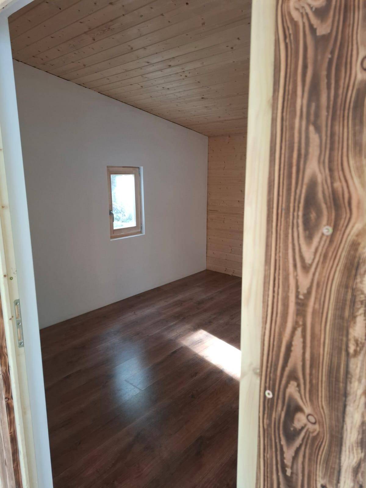 Eingangsbereich zum Innenraum mit rustikalem Holztürrahmen, Laminatboden und Blick auf ein Fenster.