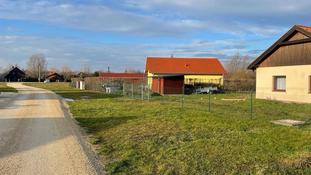 Ländliche Straße mit angrenzenden Grundstücken und Häusern unter blauem Himmel.