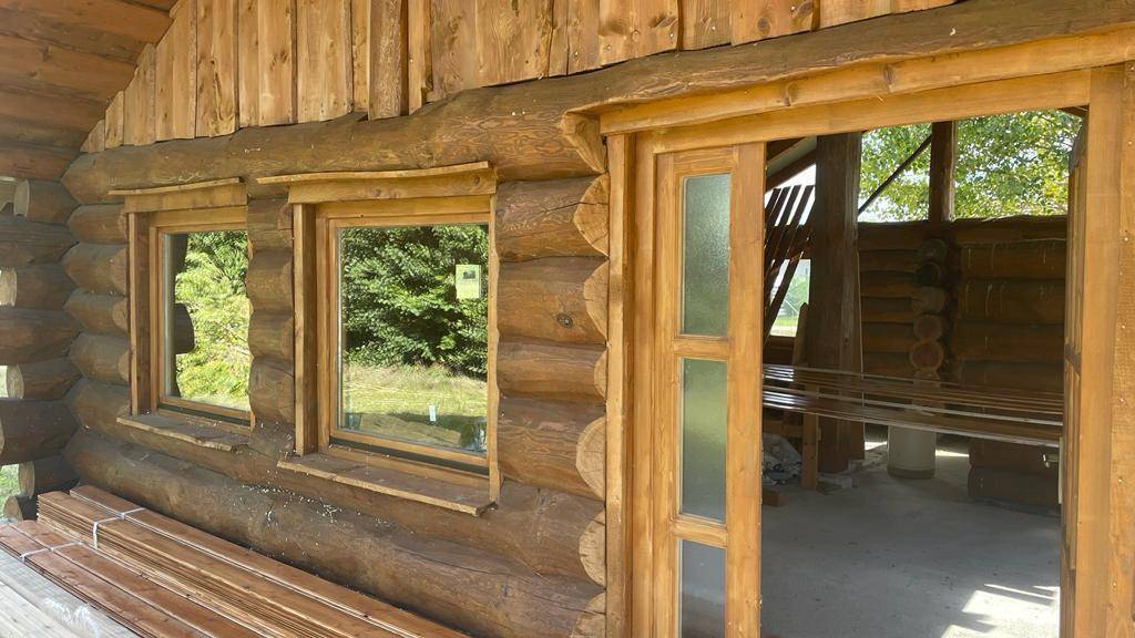 Überdachter Eingangsbereich des Blockhauses mit Holztür, Fenstern und einem rustikalen Holzpfosten.