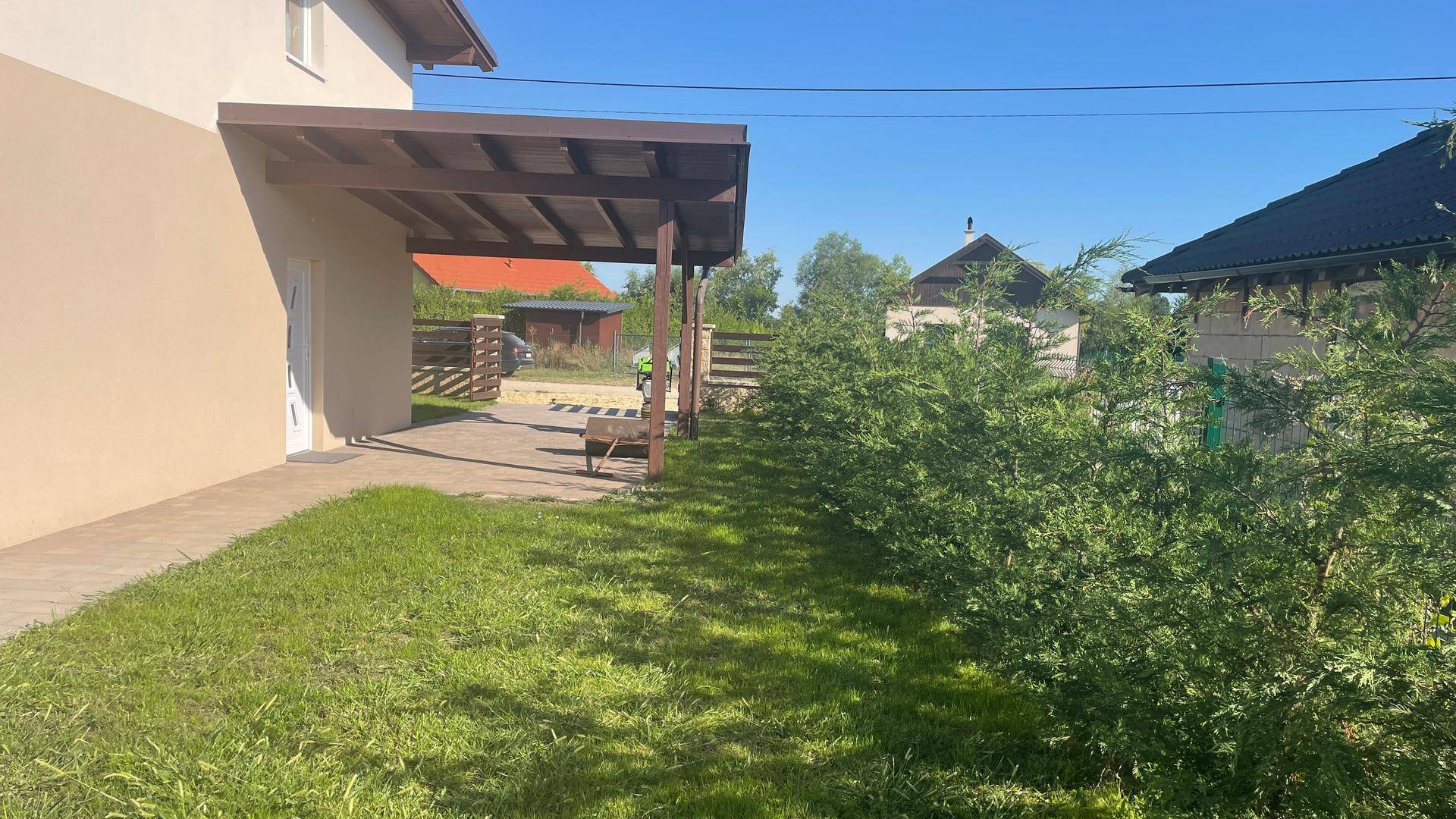 Gartenbereich mit Rasen und Carport, umgeben von Hecken.