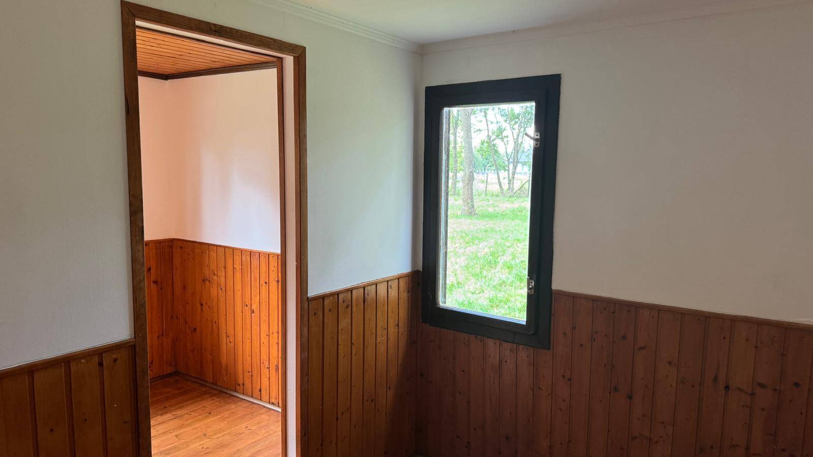 Innenraum mit Holzvertäfelung und einem Fenster, das den Blick auf die grüne Umgebung freigibt.