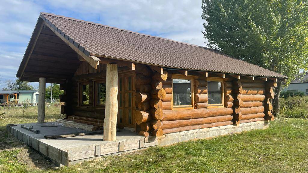 Rustikales Blockhaus mit überdachter Veranda und Blick auf die umliegende Natur und den See.