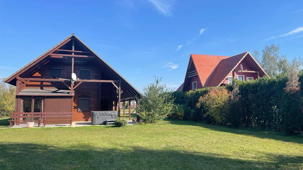 Holzhaus mit großem Rasen und Nachbarhaus mit rotem Dach, umgeben von Hecken.