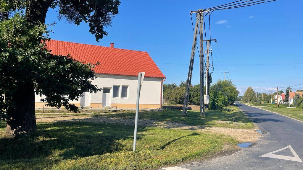 Seitenansicht des Hauses mit rotem Dach und weißer Fassade, umgeben von Bäumen und einer Straße.