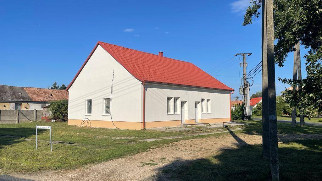 Das Haus mit rotem Dach und weißer Fassade, umgeben von einem großen Grundstück und Stromleitungen.