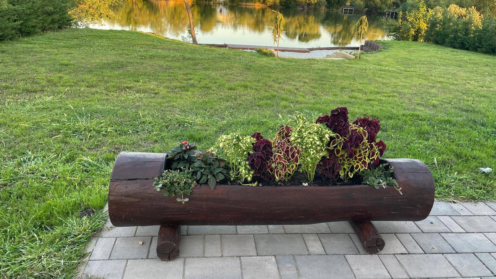Blumenkübel aus Holzstamm im Garten mit Blick auf den See.