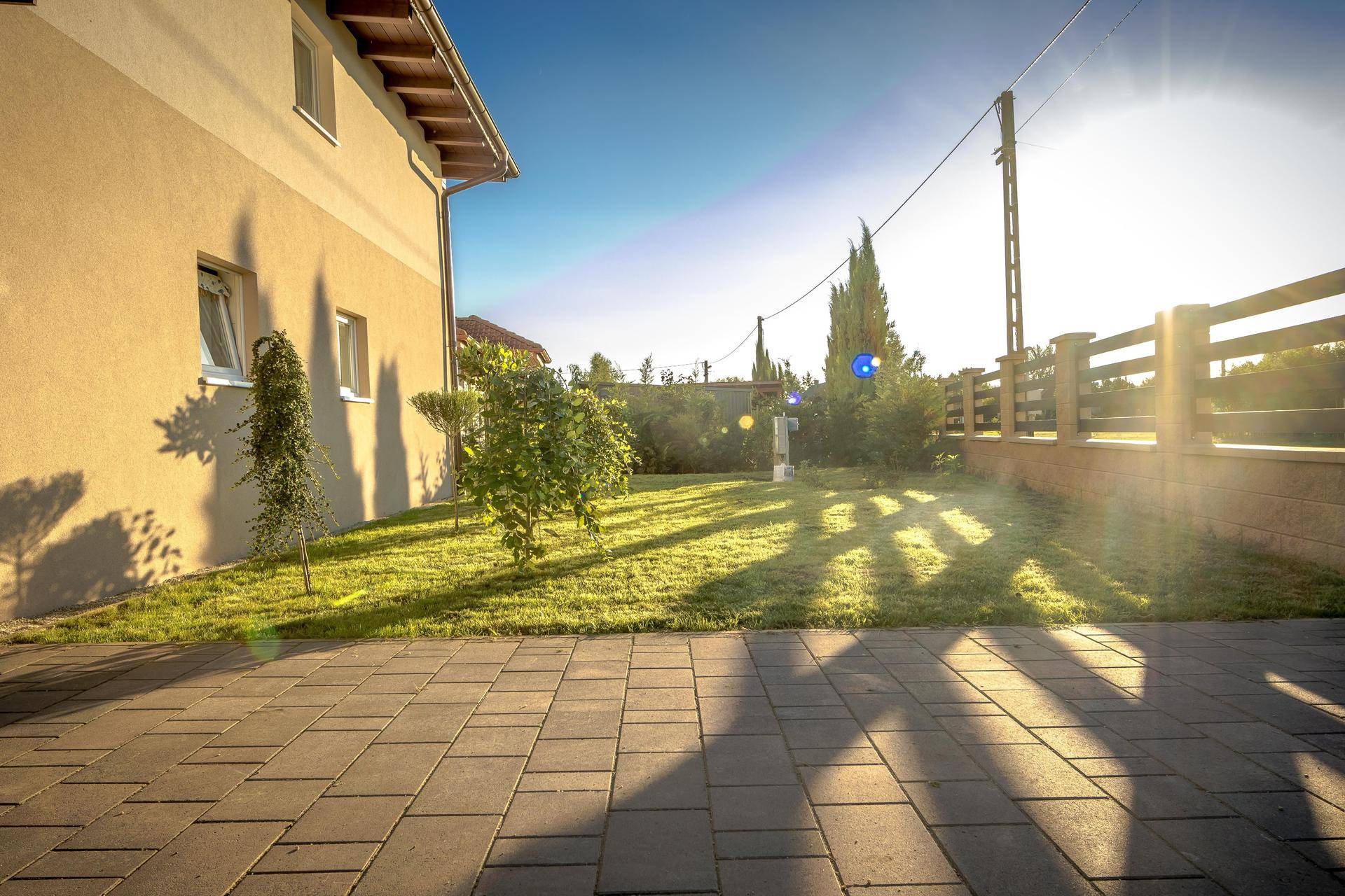 Sonnige Seitenansicht des Hauses mit gepflastertem Weg und gepflegtem Rasen.
