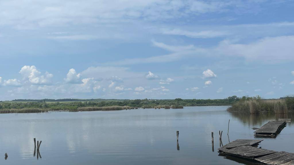 Ruhiger See mit verfallenen Holzstegen im Wasser und einem weiten Himmel.