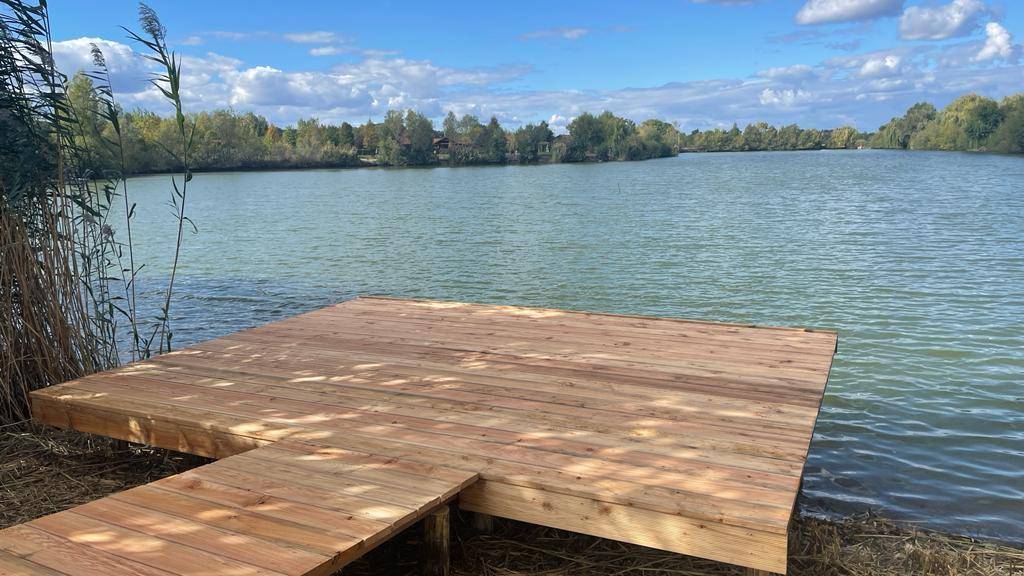 Neuer Holzsteg am Seeufer, ideal für Angler oder zum Entspannen am Wasser unter blauem Himmel.