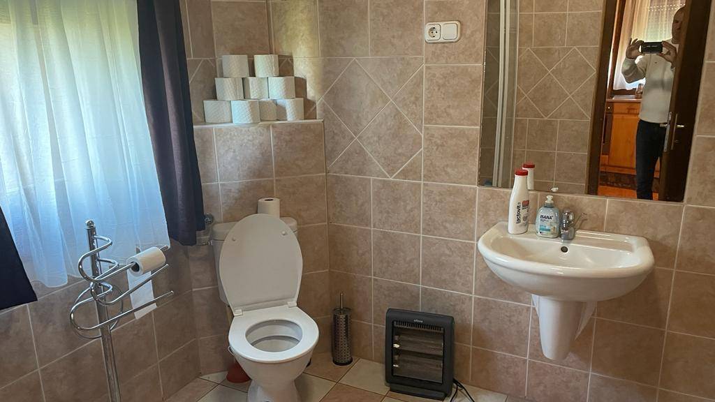 Funktionales Badezimmer mit beigefarbenen Fliesen, Toilette, Waschbecken und Fenster.