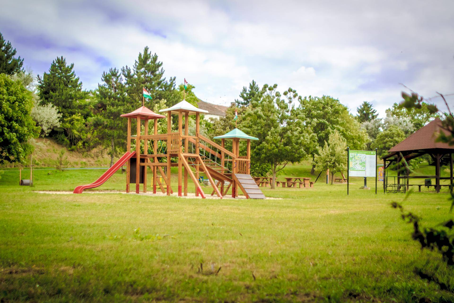Großer Spielplatz mit Holzspielgeräten und viel Grünfläche für Kinder.