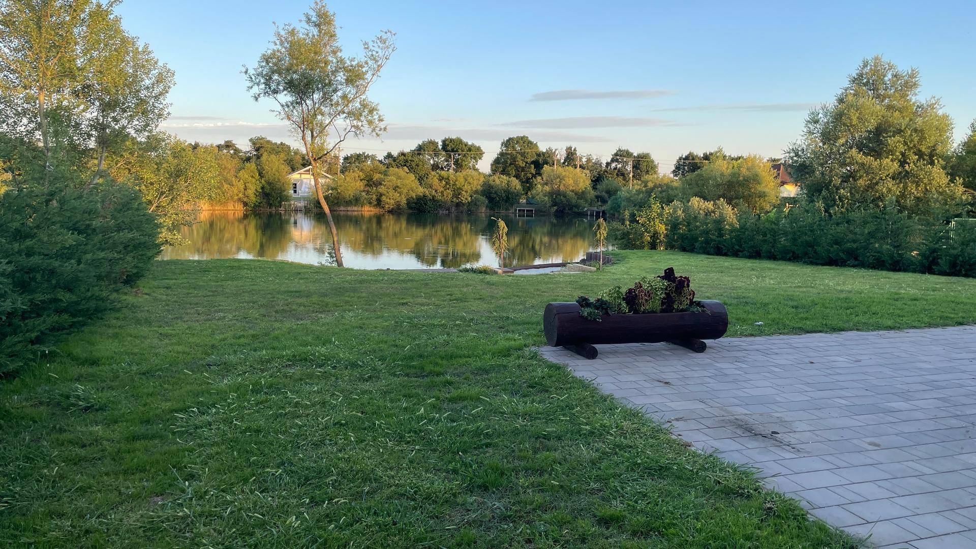 Gartenbereich mit Rasen, Blumenkübel und Blick auf den See.