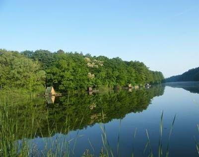 Friedlicher See mit bewaldeten Ufern und kleinen Hütten am Wasser unter klarem Himmel.