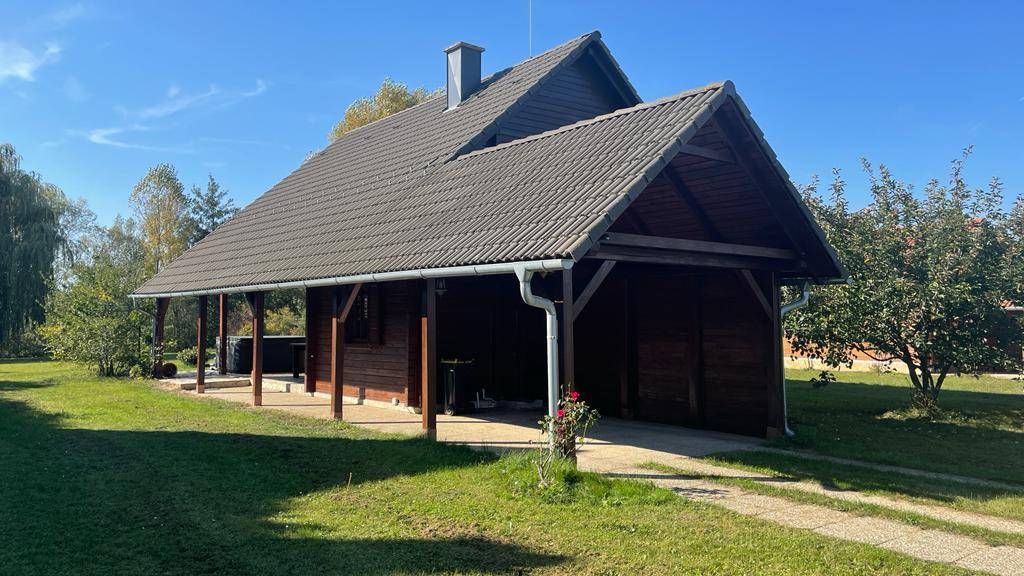 Seitenansicht des Holzhauses mit Satteldach und überdachtem Bereich, umgeben von Grün.