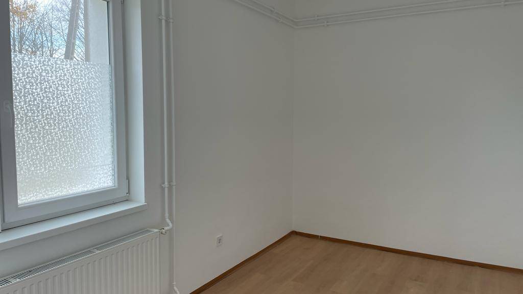 Heller Raum mit Laminatboden, weiß gestrichenen Wänden und einem großen Fenster mit Heizkörper.