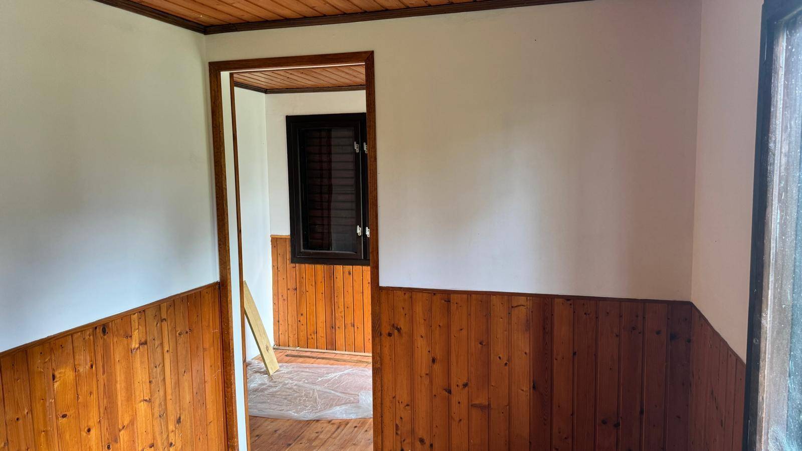 Innenraum mit Holzvertäfelung an den Wänden und einem Fenster mit Blick ins Grüne.