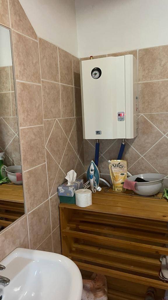 Badezimmerbereich mit Waschbecken, Spiegel und wandmontiertem Durchlauferhitzer.