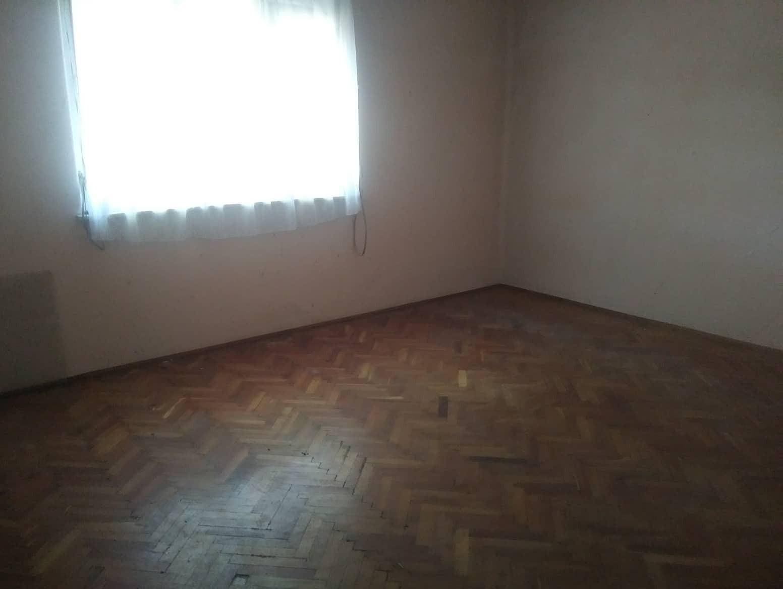 Leeres Zimmer mit Fischgrätparkett und hellem Fenster, das viel natürliches Licht hereinlässt.