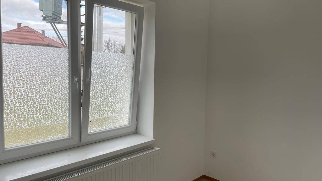 Heller Raum mit Laminatboden, weiß gestrichenen Wänden und einem großen Fenster mit Heizkörper.