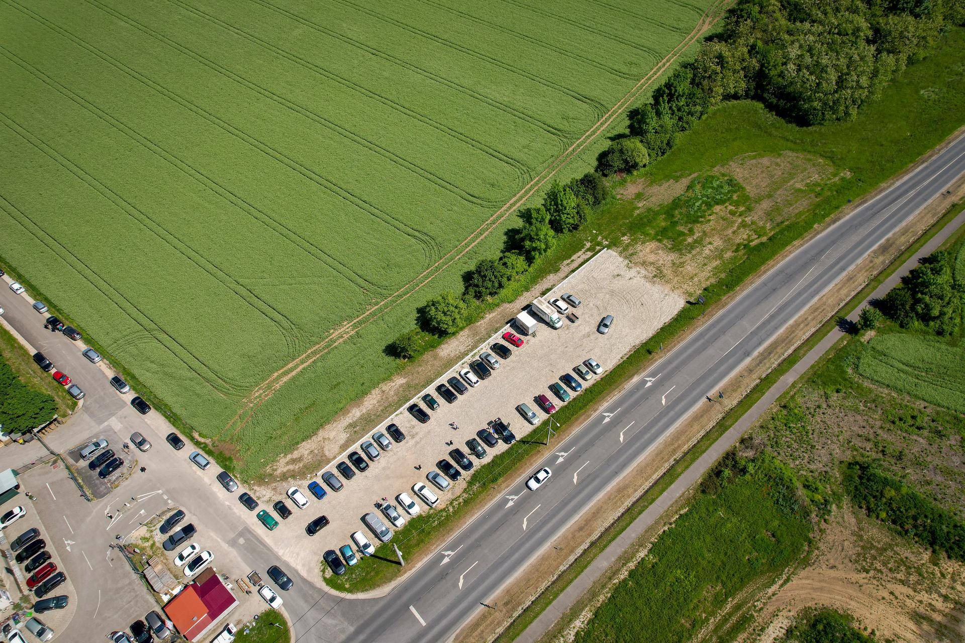 Luftaufnahme einer Straße mit Parkplätzen und weiten grünen Feldern in der ländlichen Umgebung.