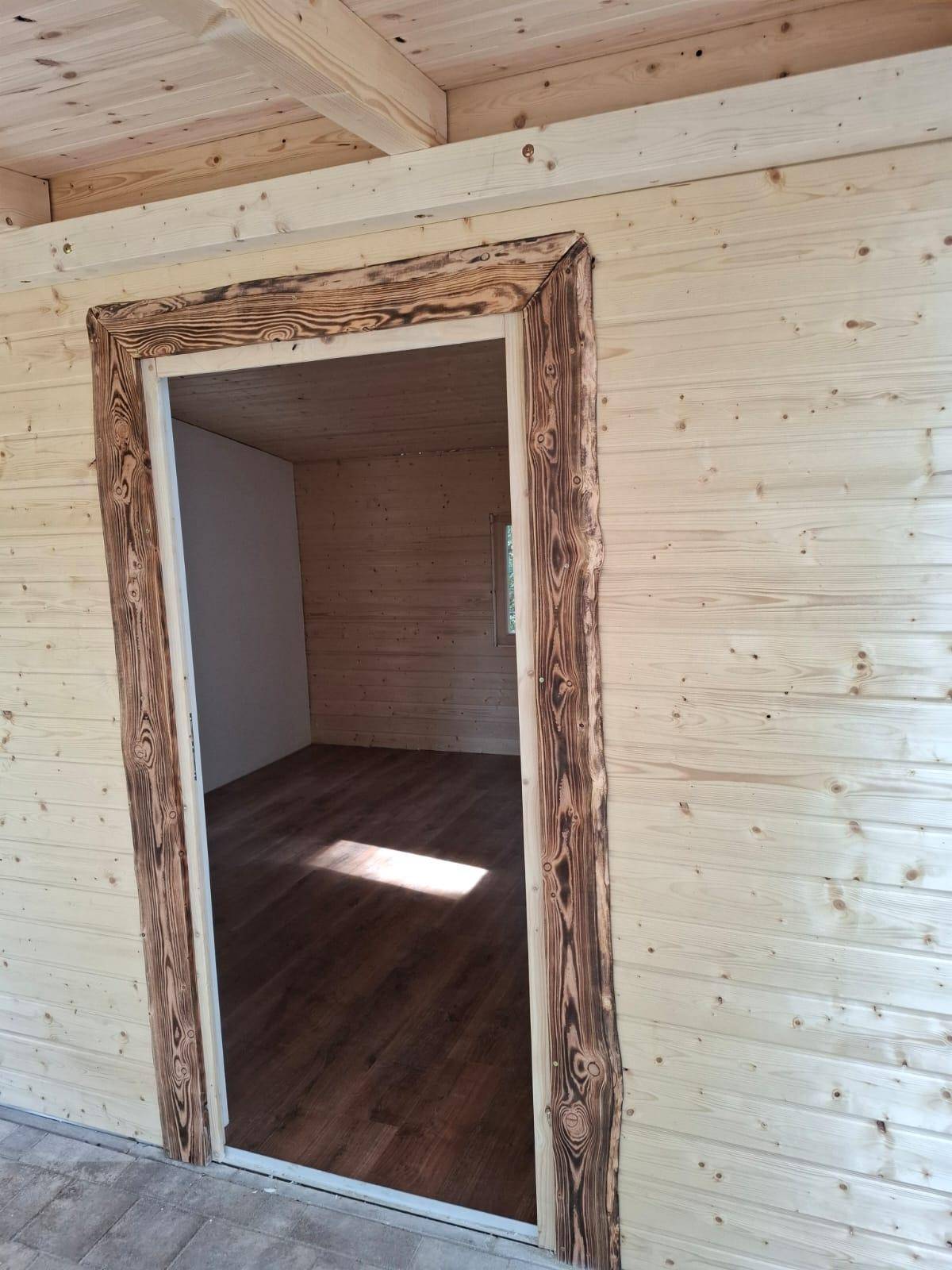 Blick vom überdachten Bereich in den Innenraum mit rustikalem Holztürrahmen und Laminatboden.
