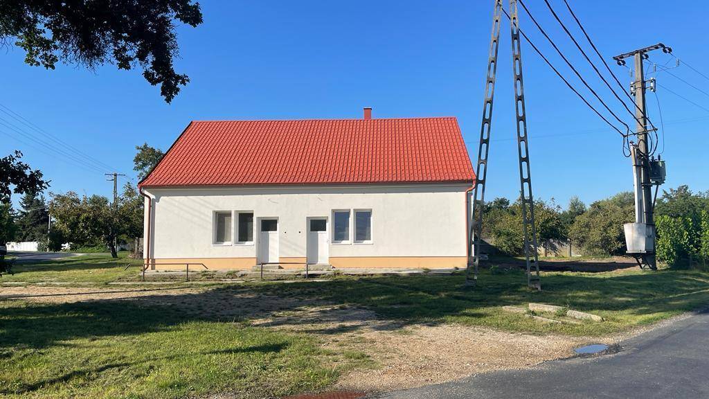 Ansicht des Hauses von der Straße mit rotem Dach und weißer Fassade in ländlicher Umgebung.