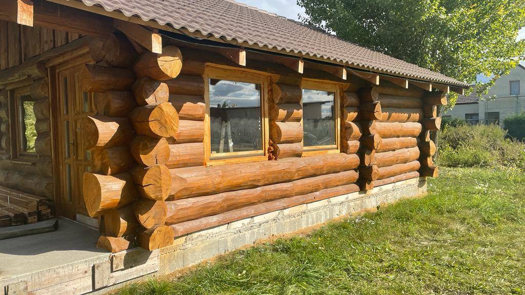 Detailansicht der Blockhausfassade mit robusten Holzstämmen und Fenstern in natürlicher Umgebung.