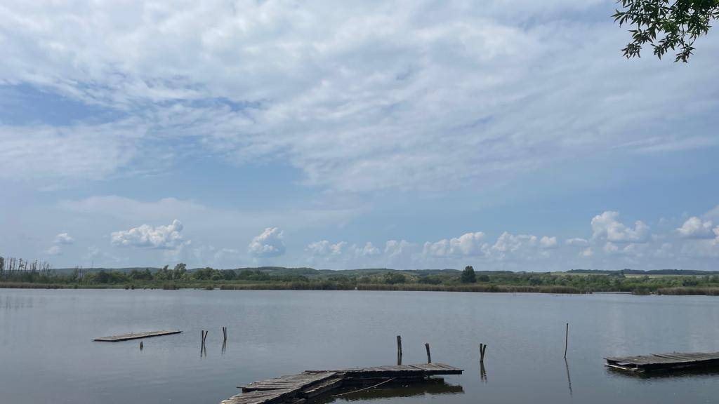 Ruhiger See mit verfallenen Holzstegen im Wasser und einem weiten Himmel.