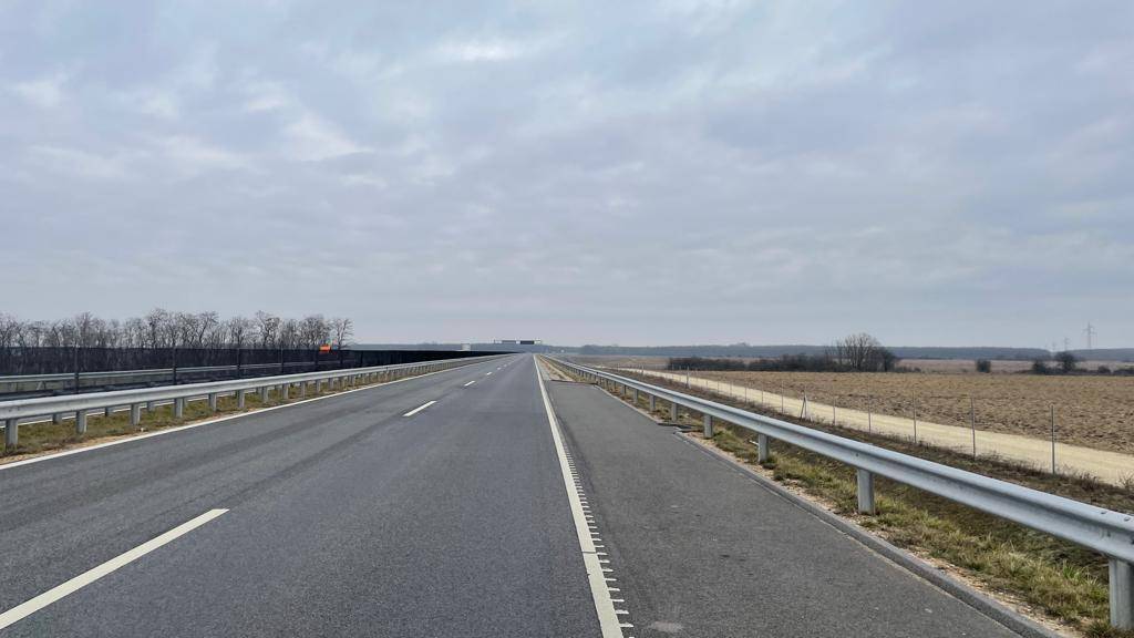 Leere Autobahnstraße neben einem weiten Feld unter bewölktem Himmel.