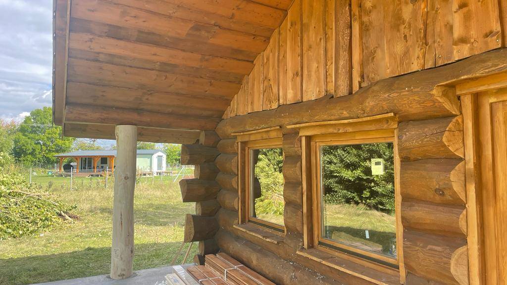 Seitenansicht des Blockhauses mit einem massiven Holzpfosten und Fenstern, die in die Natur blicken.
