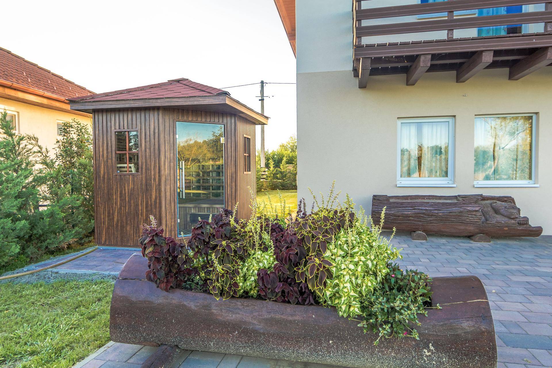 Holzsauna im Garten mit Blumenkübeln und gepflastertem Bereich.
