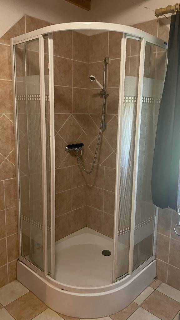 Eckduschkabine mit Glastüren und beigefarbenen Fliesen im Badezimmer.