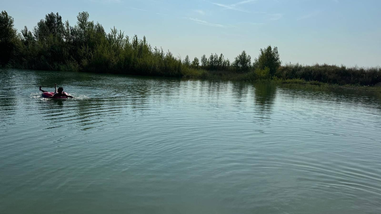 Person auf einem Schwimmreifen im ruhigen See, umgeben von grünen Bäumen am Ufer.