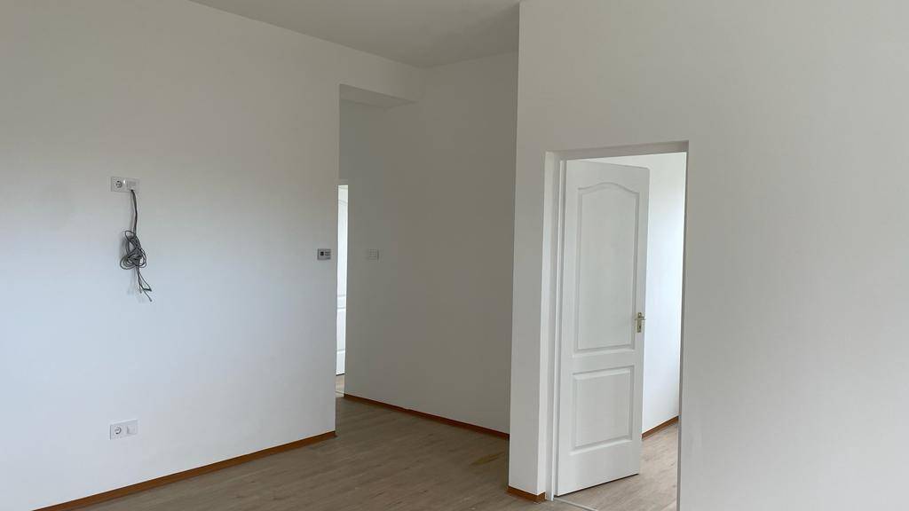 Unmöblierter Raum mit weißen Wänden, Laminatboden und sichtbaren Elektroinstallationen.