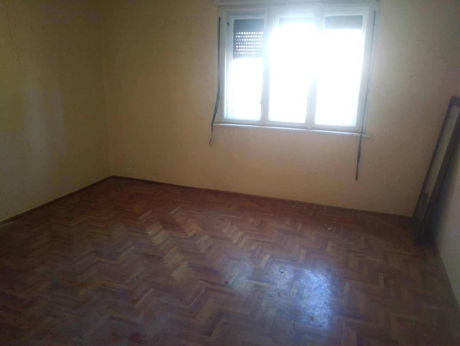 Helles Zimmer mit Parkettboden und Fenster mit Rollladen, das auf Renovierungsbedarf hinweist.
