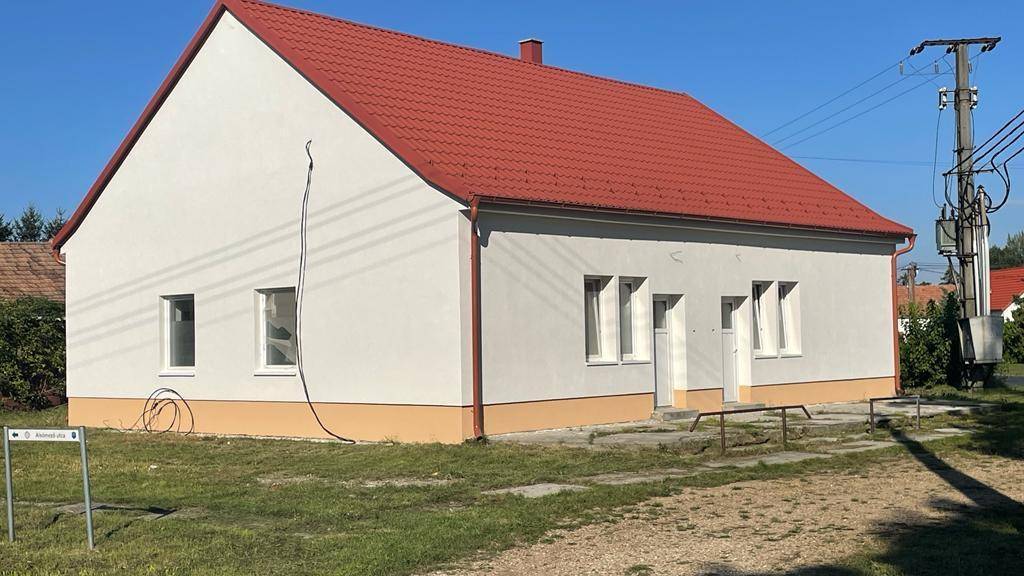 Das Haus mit rotem Dach und weißer Fassade, umgeben von einem großen Grundstück und Stromleitungen.