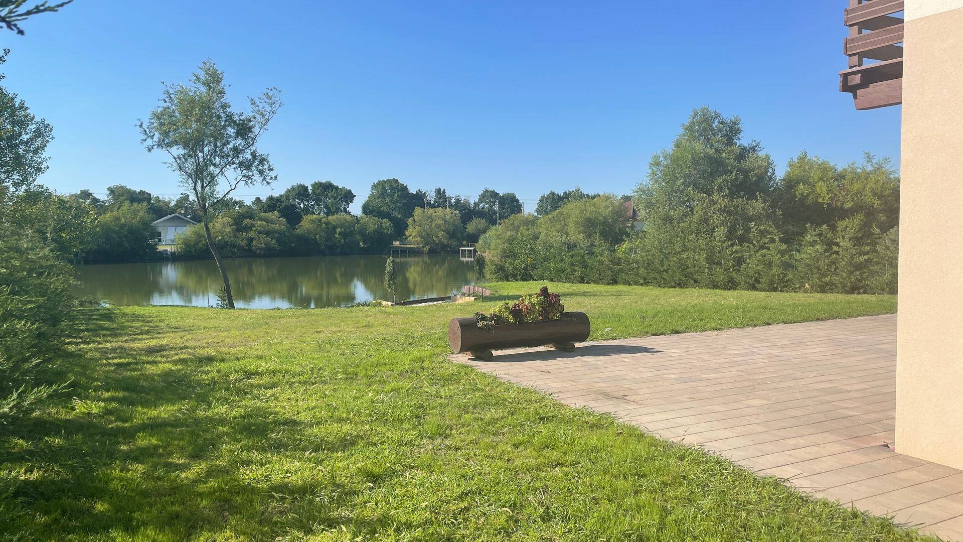 Gartenbereich mit Rasen, gepflastertem Weg und Blick auf den See.