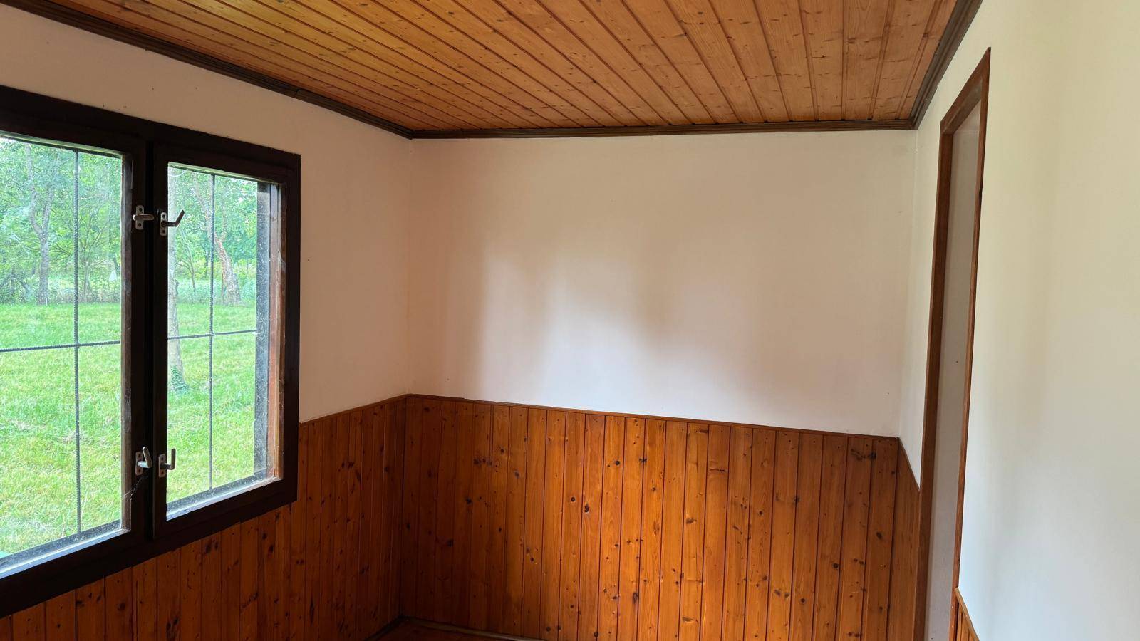 Raum mit Holzdecke und Holzvertäfelung, ein Fenster bietet Ausblick ins Grüne.