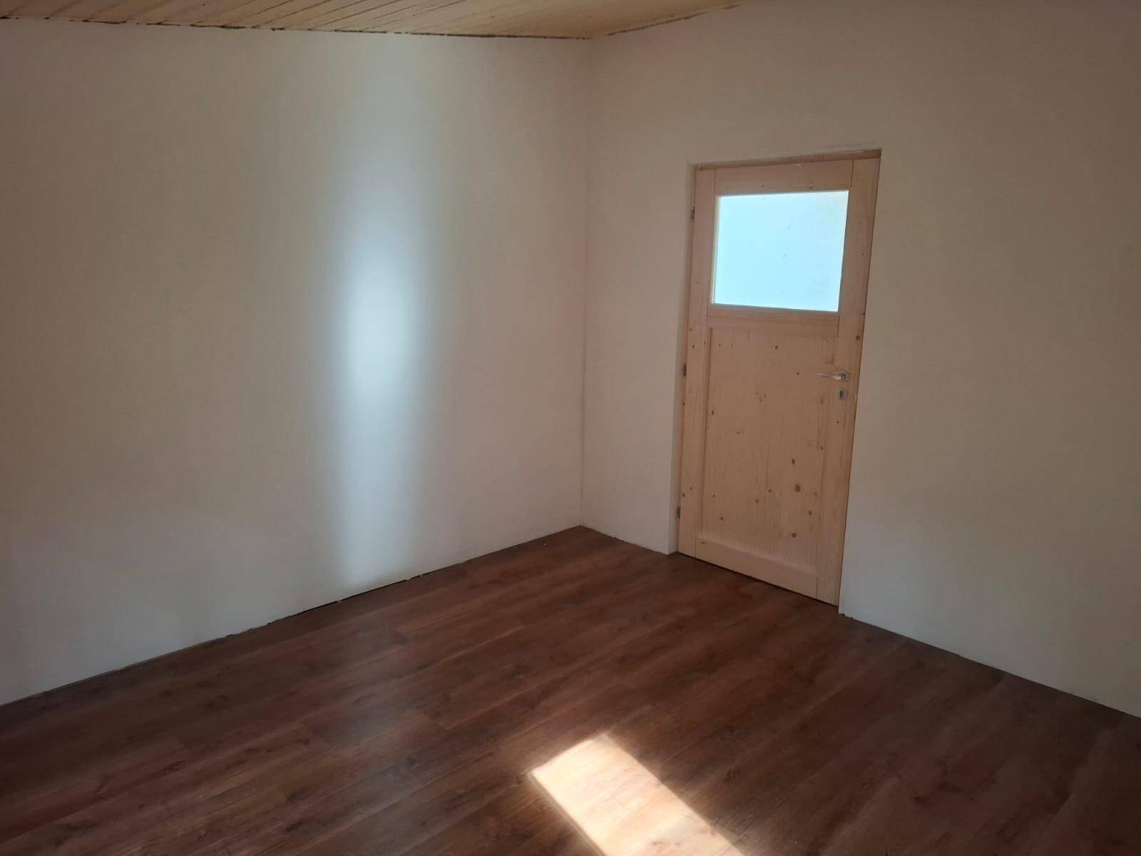 Unmöblierter Raum mit weißen Wänden, Holztür mit Glaseinsatz und Laminatboden, bereit zum Einrichten.
