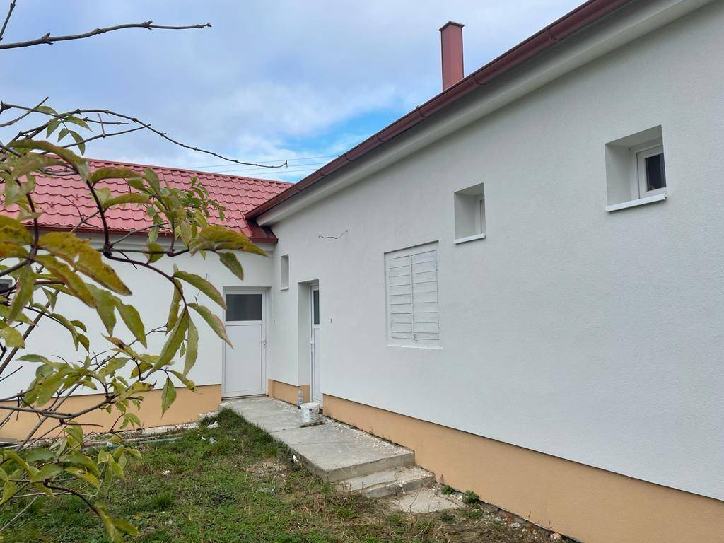 Seitenansicht des Hauses mit weißer Fassade, rotem Dach und einem kleinen Eingangsbereich.