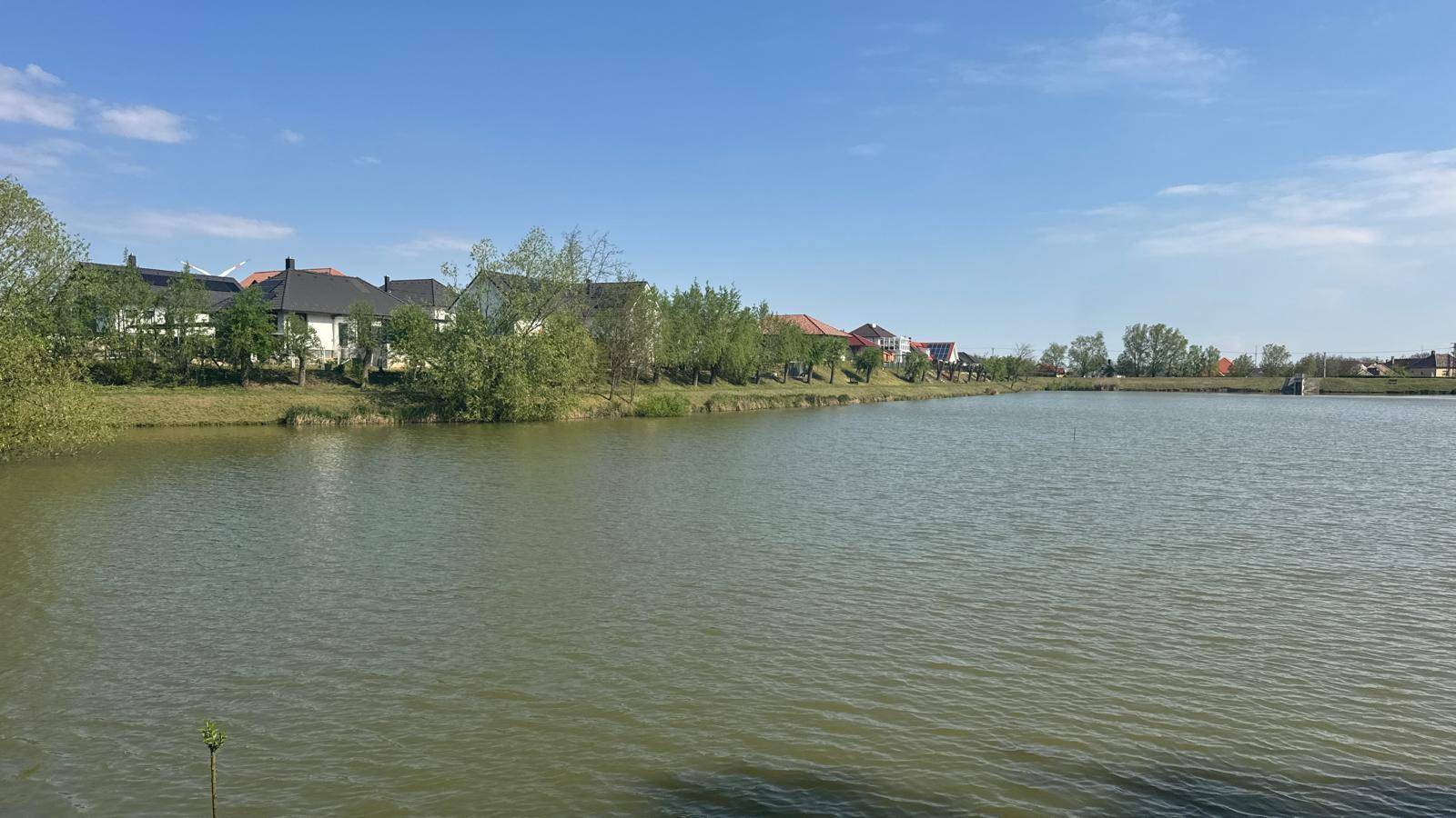 Weitläufiger See mit Häusern am gegenüberliegenden Ufer unter einem klaren blauen Himmel.
